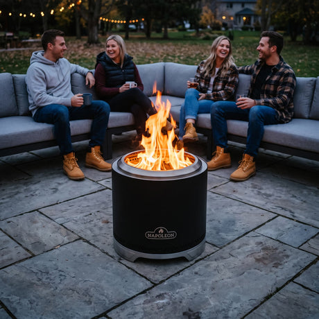 Napoleon Timberwolf 18-Inch Fire Pit in Matte Black on a stone patio with friends on an outdoor sectional at dusk