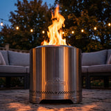 Napoleon Timberwolf 18-Inch Fire Pit in Stainless Steel lit on a stone patio at twilight