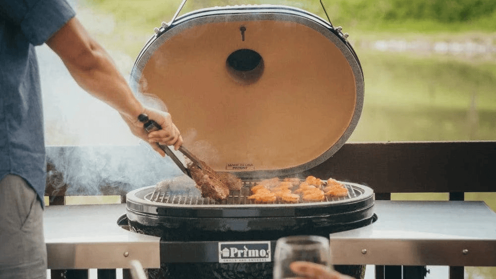 A person grilling on a portable Primo grill outdoors