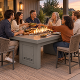 Friends passing dishes at a backyard dinner around a Top Fires Alameda 72-inch composite wood gas fire table with a Tacoma tabletop and Gray base