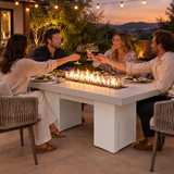 Couples toasting at a dinner party around a Top Fires Alameda 72-inch GFRC gas fire table with a Limestone tabletop and White base