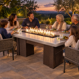 Family enjoying an evening meal around a Top Fires Alameda 72-inch GFRC gas fire table with a Metallic Pearl tabletop and Copper Vein base