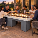 Friends passing dishes at a backyard dinner around a Top Fires Alameda 72-inch GFRC gas fire table with a Metallic Pearl tabletop and Gray base