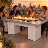 Friends enjoying tapas and cocktails on a rooftop terrace around a Top Fires Alameda 72-inch GFRC gas fire table with a Metallic Pearl tabletop and White base