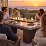 Friends dining on a beach house deck at sunset around a Top Fires Alameda 72-inch GFRC gas fire table with a Metallic Silver tabletop and Copper Vein base