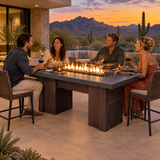Friends dining on a desert modern patio at dusk around a Top Fires Alameda 72-inch GFRC gas fire table with a Metallic Slate tabletop and Copper Vein base