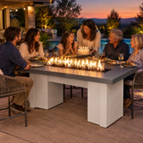 Family celebrating a birthday dinner on a poolside patio around a Top Fires Alameda 72-inch GFRC gas fire table with a Metallic Slate tabletop and White base