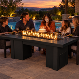 Family celebrating a birthday dinner on a poolside patio around a Top Fires Alameda 72-inch GFRC gas fire table with a Smooth Black tabletop and Black base