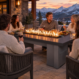 Family dinner on a mountain lodge patio at dusk around a Top Fires Alameda 72-inch GFRC gas fire table with a Smooth Black tabletop and Gray base