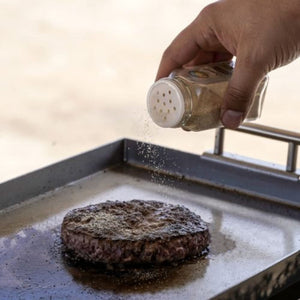 seasoning a patty on the top fires the overlander portable grill